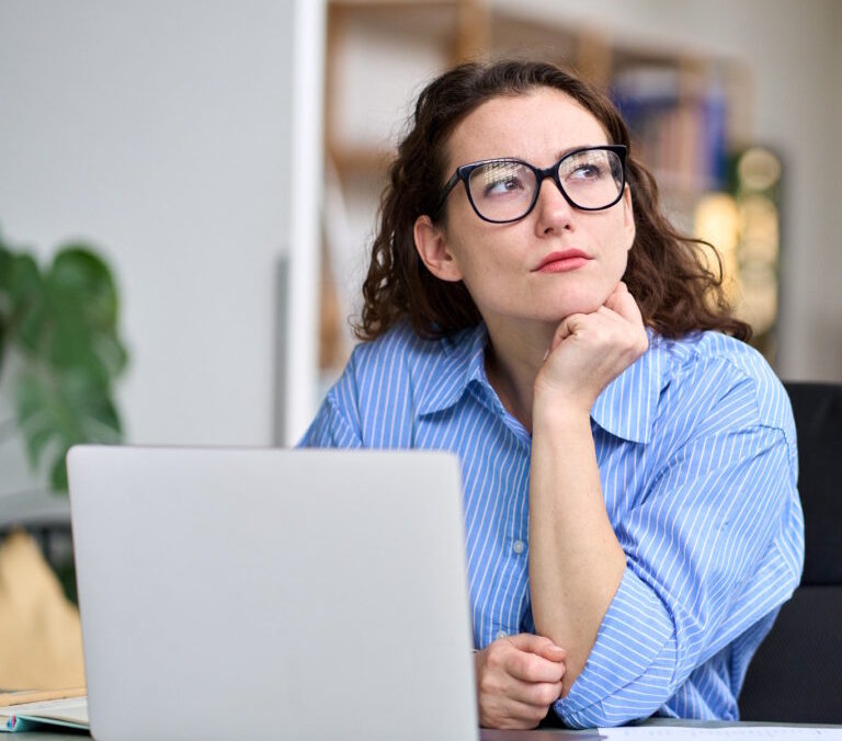 Thoughtful serious professional business woman employee or student using laptop, looking away thinking of question or idea, working or learning on computer feeling doubt, at home or in office.